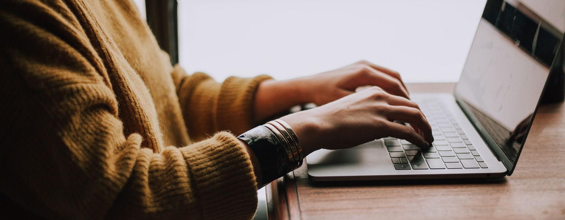 woman types on her laptop near large window